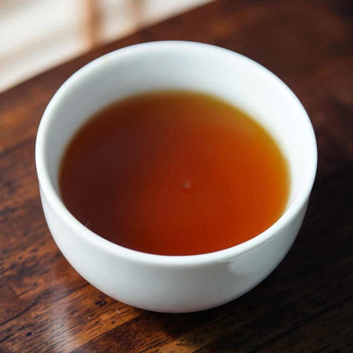 A white ceramic cup filled with amber-brown tea, set on a dark wooden table.