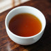 A white ceramic cup filled with amber-brown tea, set on a dark wooden table.