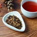Loose leaf tea in a white dish with a cup of brewed tea on a wooden table.