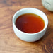 A small white ceramic cup filled with amber-brown tea, placed on a wooden tabletop.