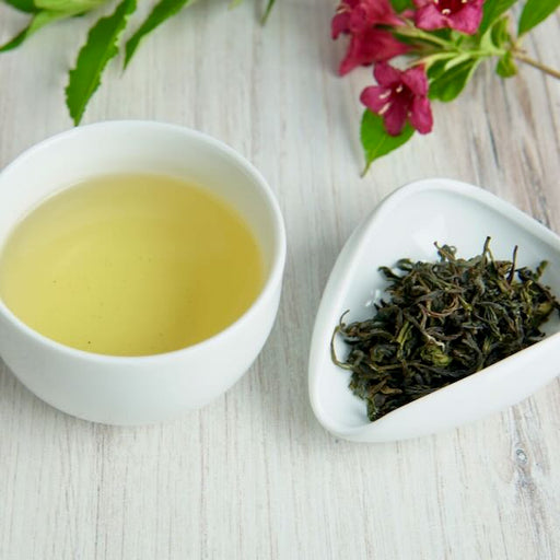 Tea cup with green tea and a bowl of green tea leaves on a wooden surface.