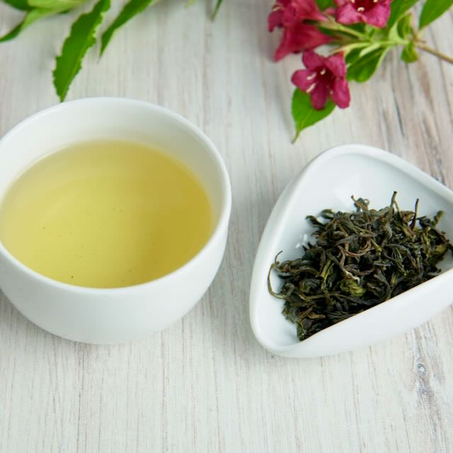 Tea cup with green tea and a bowl of green tea leaves on a wooden surface.