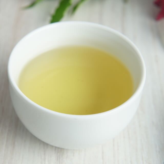 White ceramic cup filled with green tea on a light wooden surface
