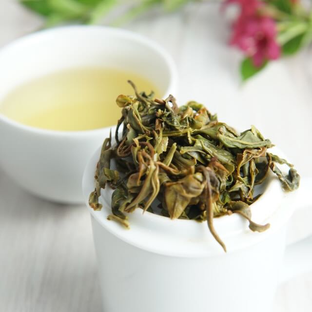 Tea leaves and a cup of tea on a white surface with a blurred background