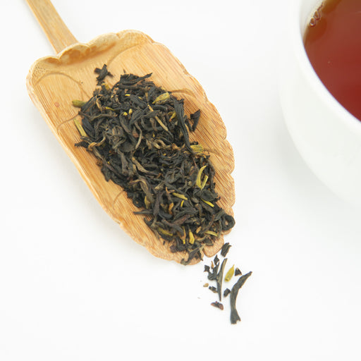 Wooden scoop filled with tea leaves on a white background