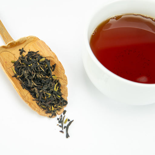 Tea leaves on a wooden scoop next to a cup of brewed tea on a white background