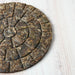 A close-up of a round compressed tea cake with visible leaf texture, placed on a light wood surface.