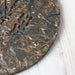 A close-up of a round compressed tea cake, showing the textured dark brown and black leafy surface, resting on a white painted wood background.