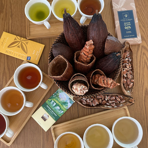 Cocoa beans and cups of tea on a wooden surface with chocolate packaging.